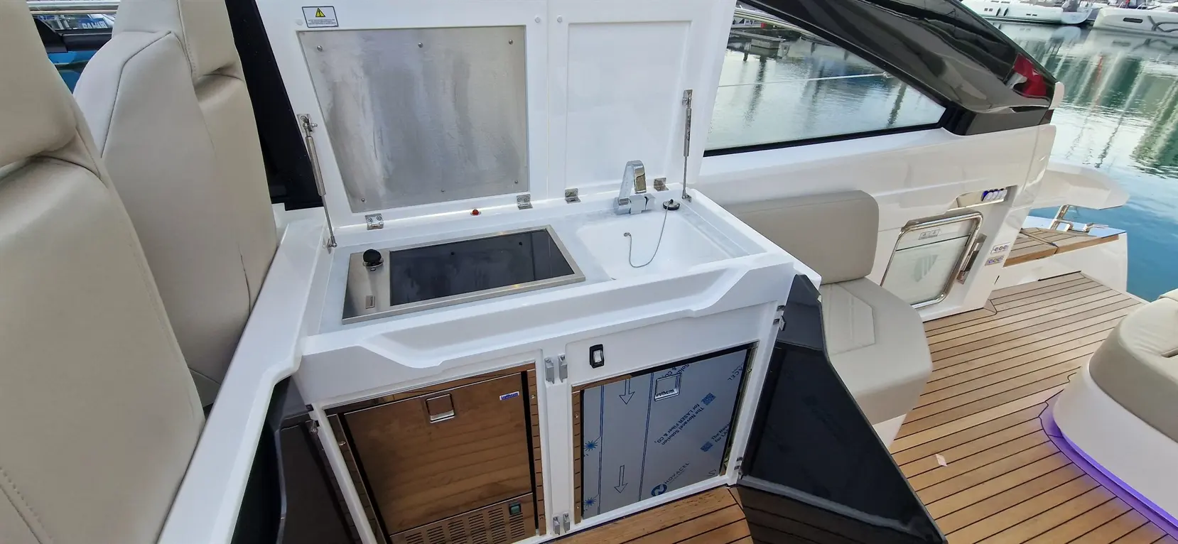 Compact boat wet bar featuring a sink, stove, and storage, with a view of the marina reflected in the water.